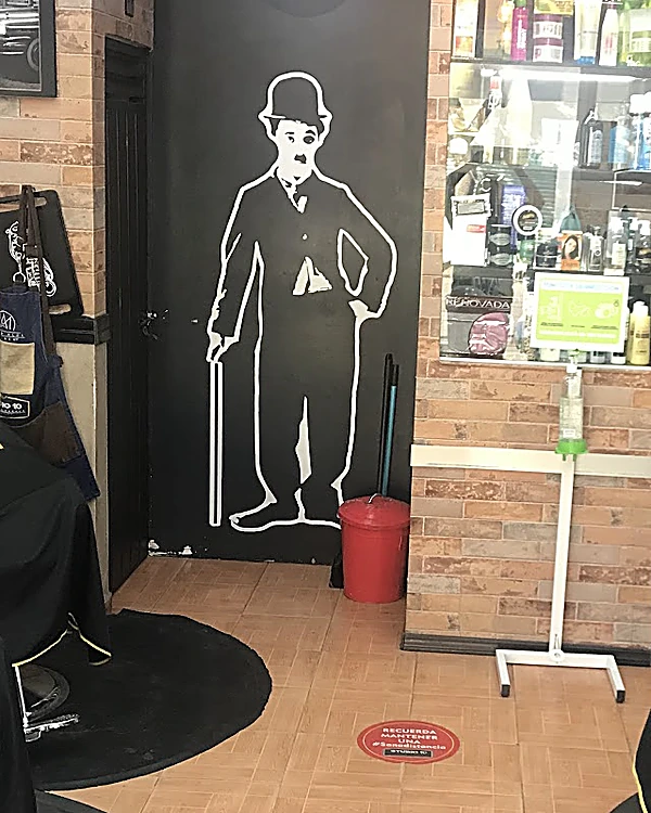 El salón de Studio 10: muro de ladrillo, sillones con capa negra y logo amarillo, la vitrina de productos y, en la pared negra, la silueta en línea blanca de un caballero de bombín y bastón