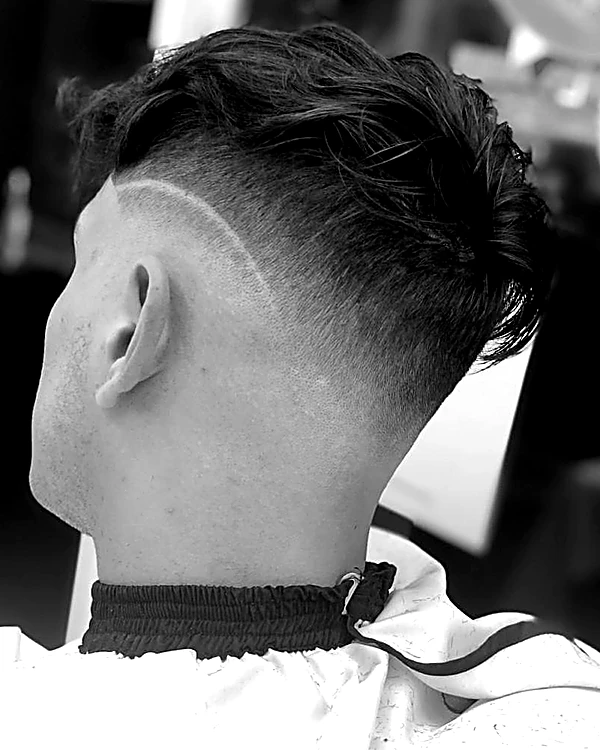 Degradado alto con una línea curva rapada sobre la oreja y textura arriba, visto desde atrás, en blanco y negro