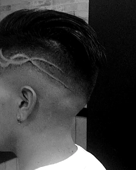 Lateral rapado con un diseño de líneas en zigzag trazado con navaja y el cabello largo peinado hacia atrás, en blanco y negro