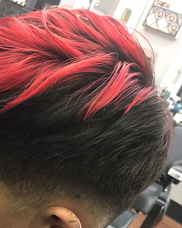 Cabello oscuro con mechas rojas peinado hacia arriba y degradado en los lados
